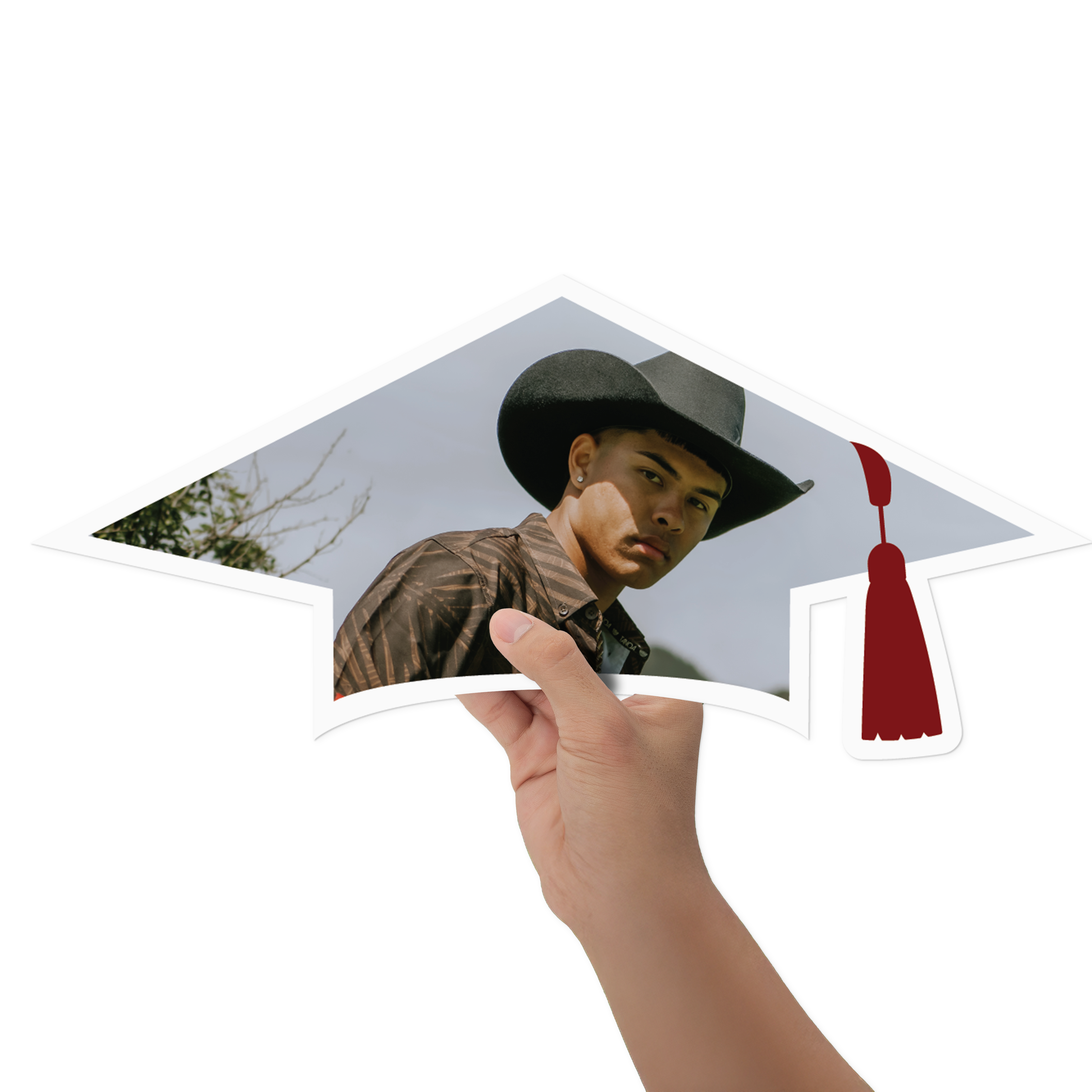 A hand holds a cutout graduation cap sign featuring a cowboy photo, with a tassel on the right side.